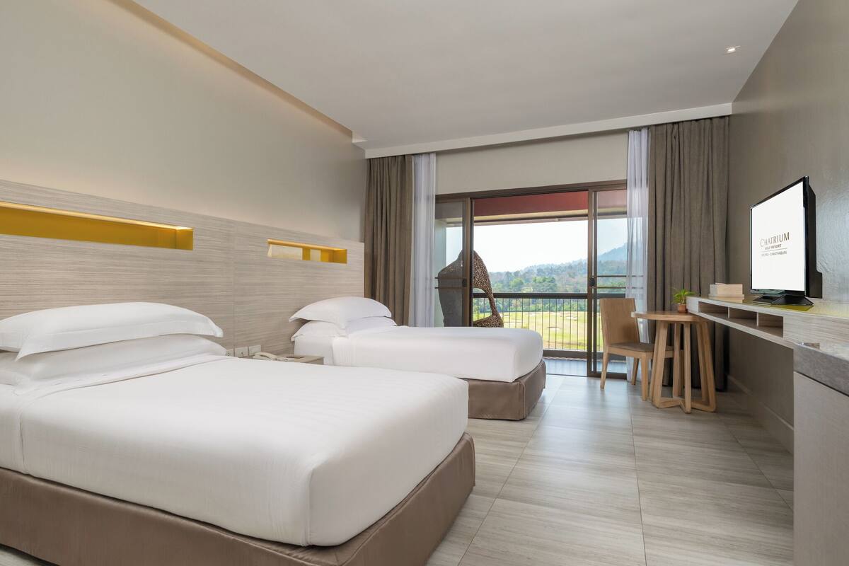 Une chambre d’hôtel avec deux lits, un bureau, une chaise, une télévision et une grande fenêtre donnant sur l’extérieur.