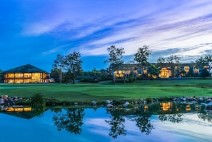 Uma propriedade grande e iluminada com vários edifícios, um gramado bem cuidado e um lago espelhado.