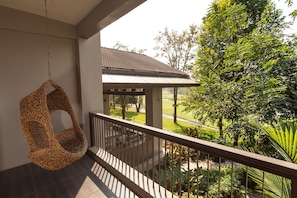 Een balkon met een hangstoel, uitzicht op een tuin en een gebouw op de achtergrond.