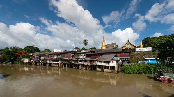 A riverside view with traditional wooden houses, a golden pagoda, and a sign for Chonburi Waterfront.