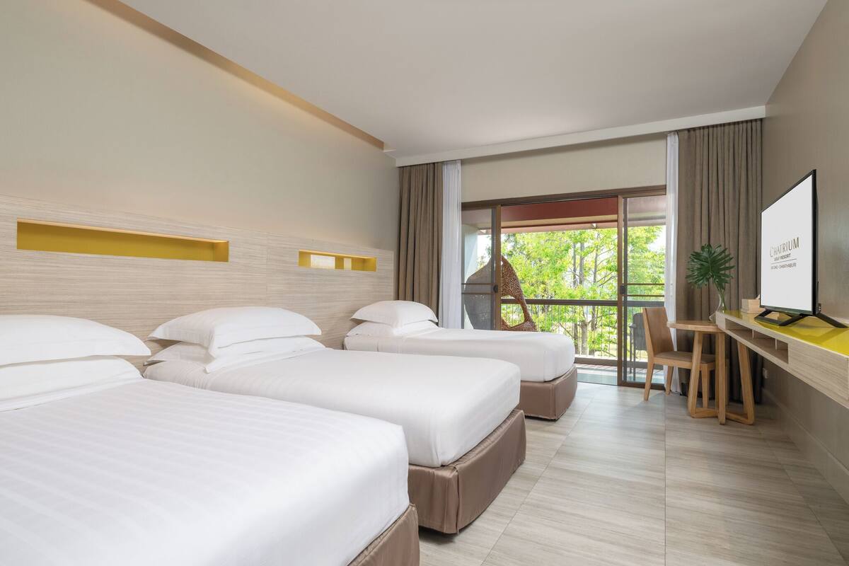 Une chambre d’hôtel avec trois lits, un bureau et une grande fenêtre.