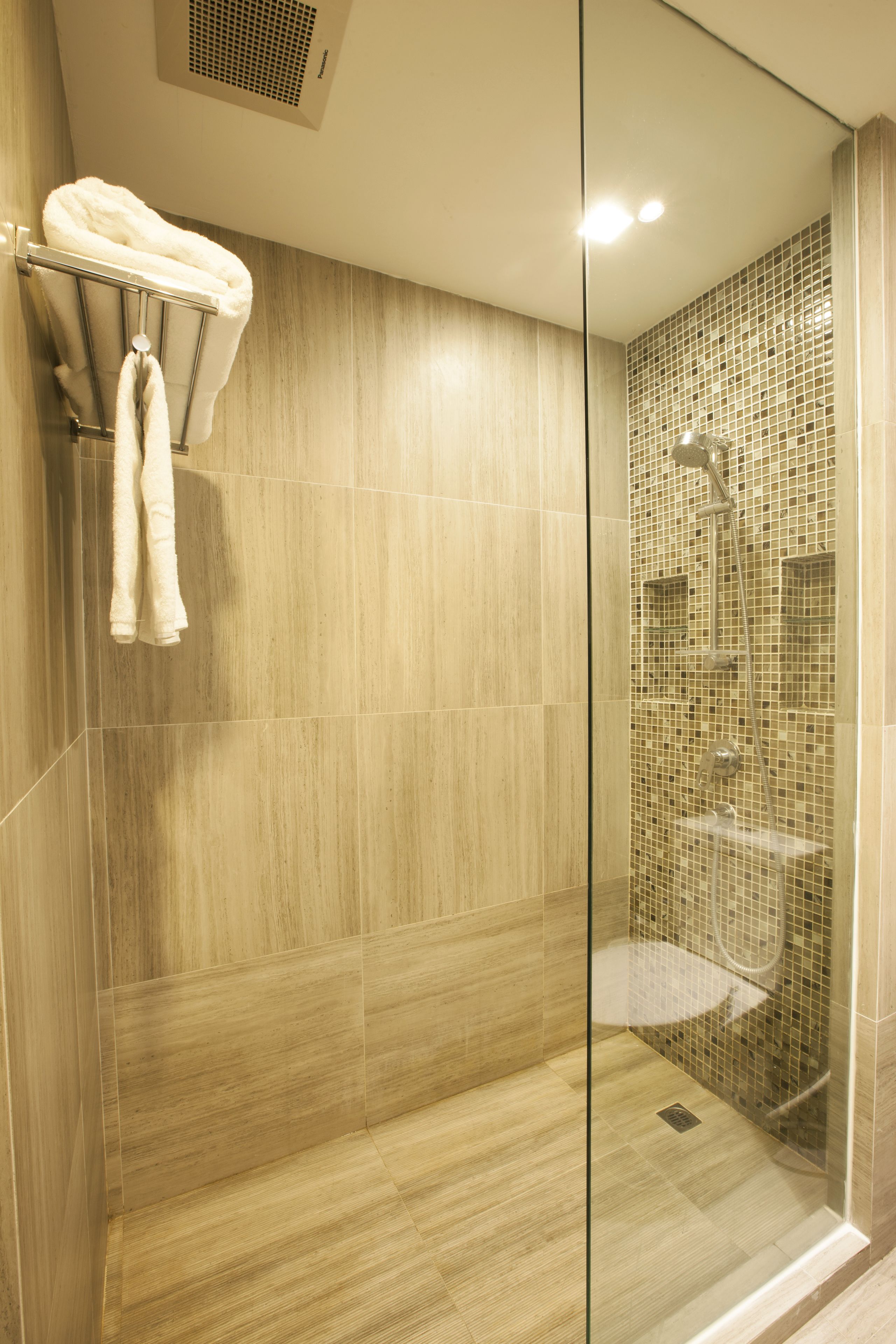A modern shower with a glass door, a towel rack with two towels, and a tiled wall.