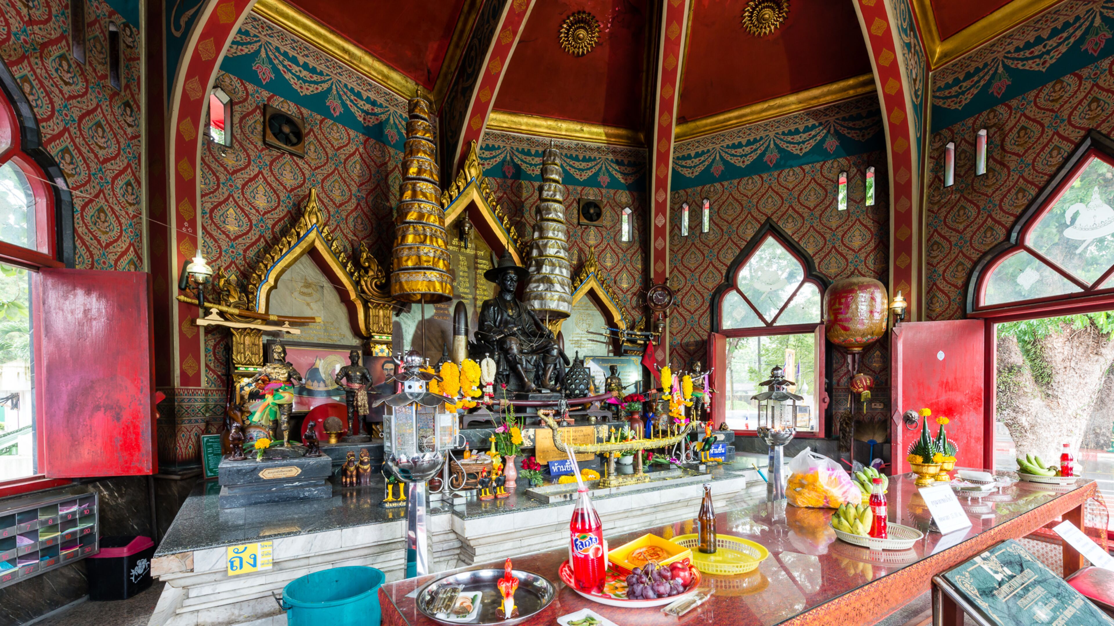 L’intérieur d’un temple, avec une statue centrale, divers objets religieux et une table où sont disposées des offrandes.