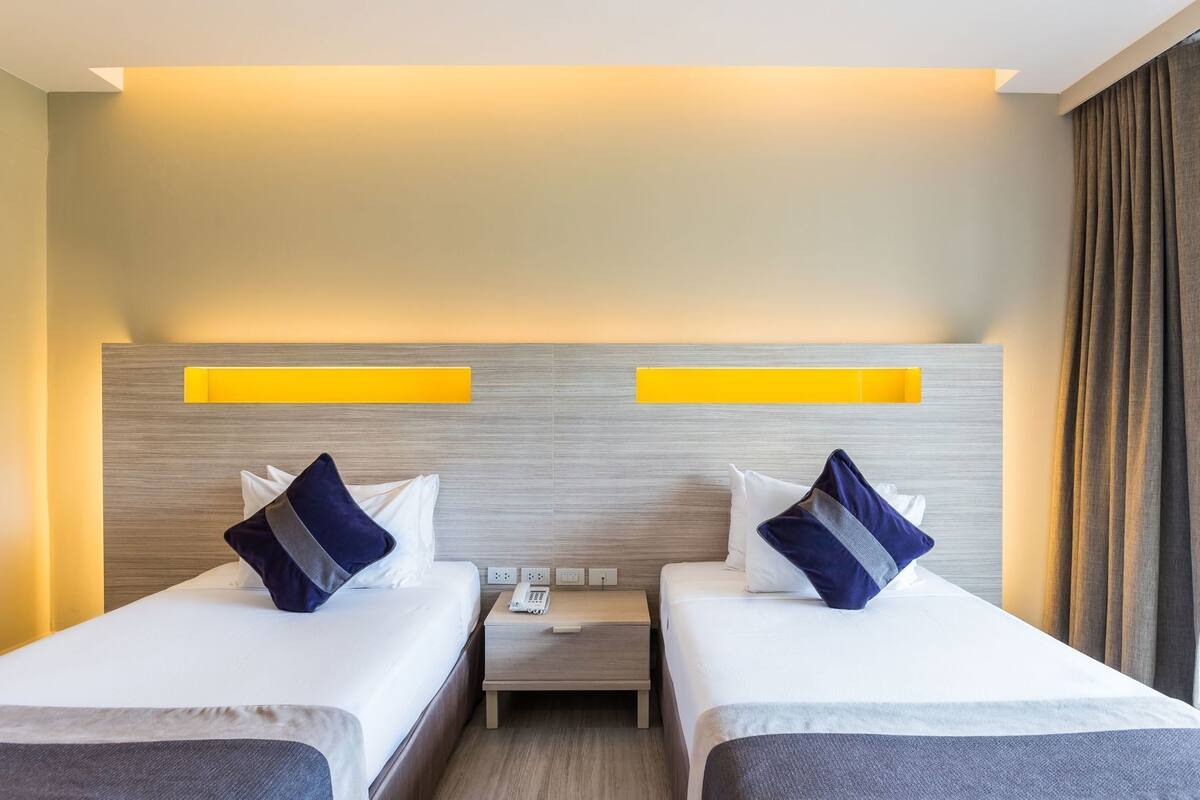 Une chambre d’hôtel avec deux lits, une table de chevet avec un téléphone et une tête de lit moderne dotée d’un éclairage intégré.