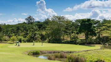 Un campo de golf con un estanque, árboles y cielo despejado.