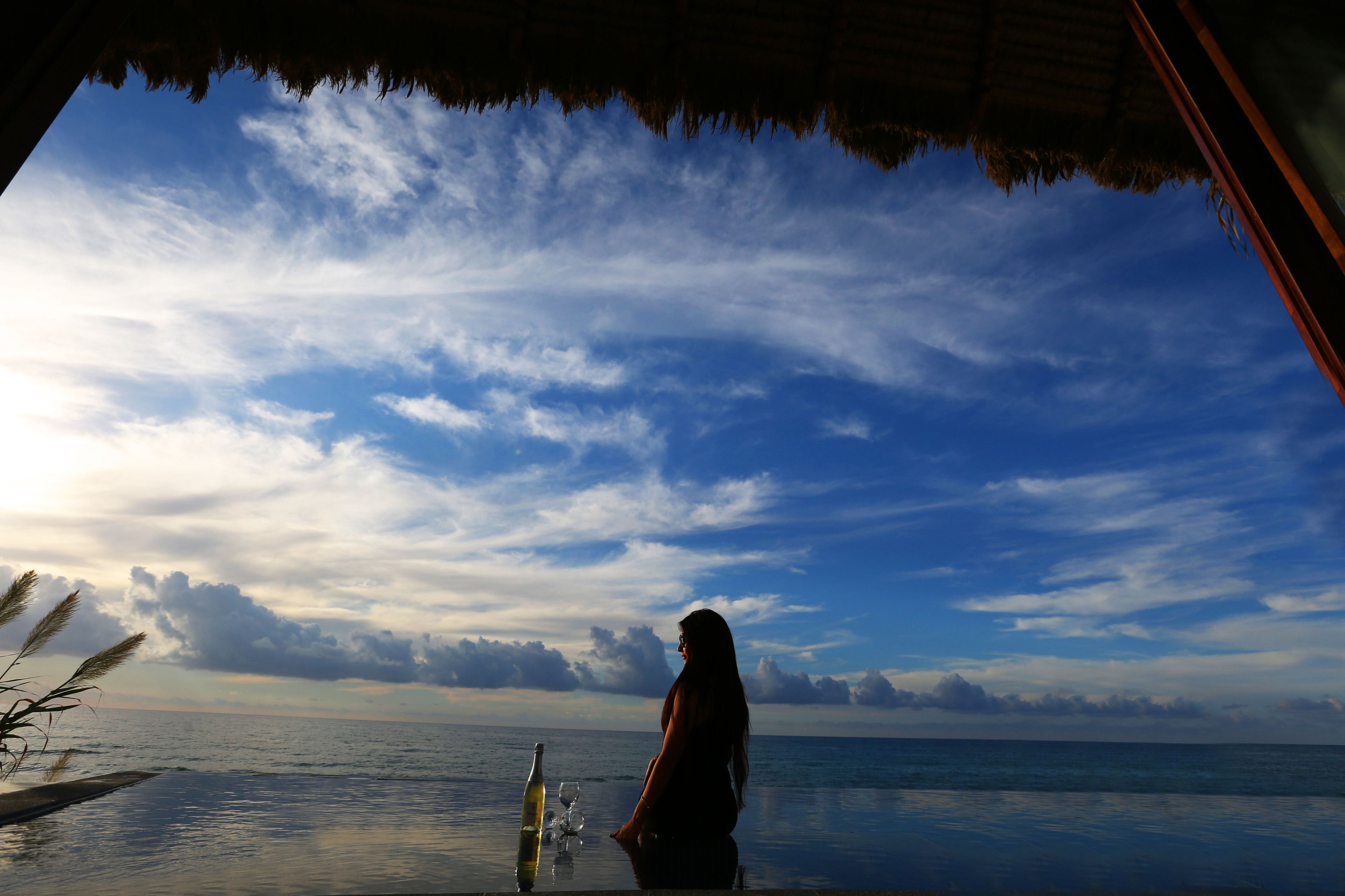 Una persona parada junto a una piscina con vista al océano y al cielo.