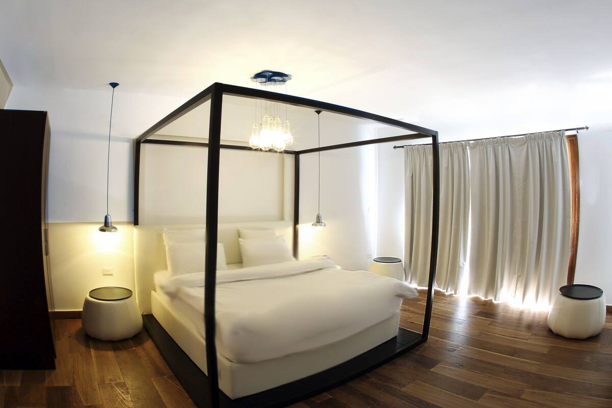 Una cama con dosel, lámparas de noche y una mesita redonda en una habitación de hotel moderna.