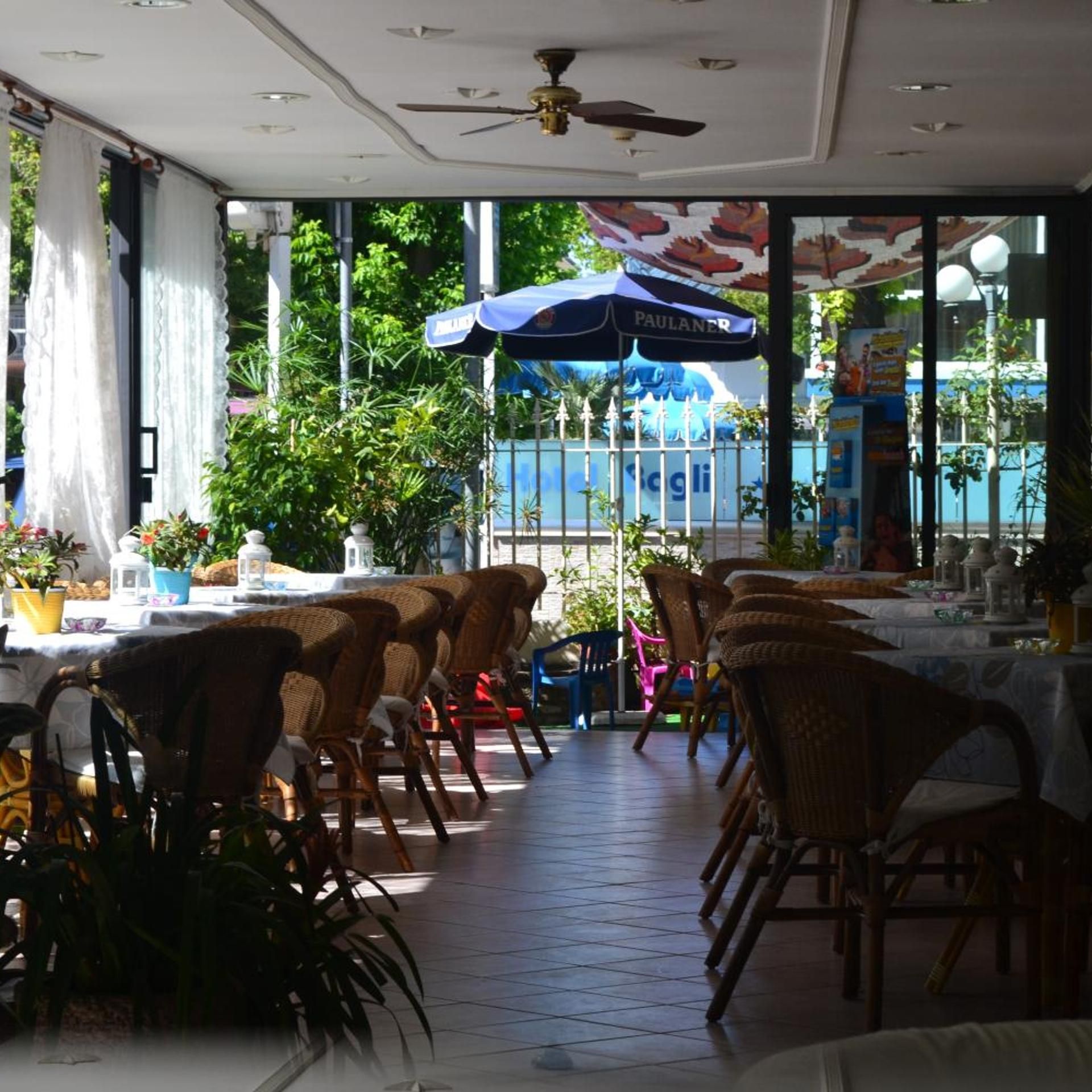 Un espace de restauration intérieur avec des chaises et des tables en osier, ainsi qu’un ventilateur de plafond.