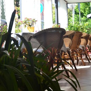 Wicker chairs arranged on a tiled patio with potted plants and a building in the background. - Hotel Alfredo's (Rimini)