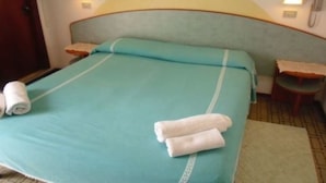 Una cama con colcha color turquesa, dos toallas enrolladas y un cabecero de madera.