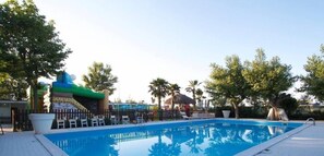 A swimming pool with a slide, surrounded by palm trees and lounge chairs. - Airone (Rimini)