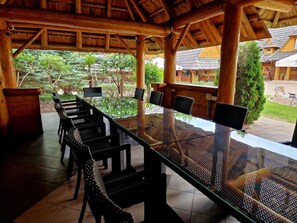 An outdoor dining area with a glass table and wicker chairs, surrounded by wooden beams and a view of the property. - Hotel Panorama (Mszczonow)