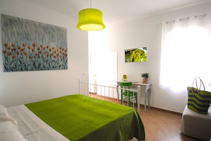 A bedroom with a bed, a desk, a chair, a television, and a painting on the wall.