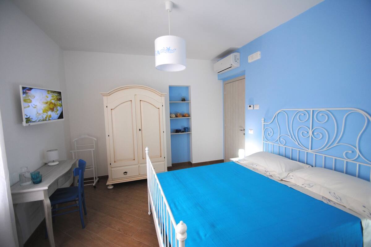 Un dormitorio con cama, escritorio, silla, armario y estante con adornos.
