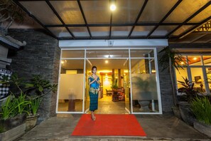 A hotel entrance with a red carpet, glass doors, and potted plants. - Mahatma Residence (Denpasar)