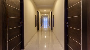 A long, narrow hallway with dark wooden doors on either side and a shiny tiled floor. - Mahatma Residence (Denpasar)