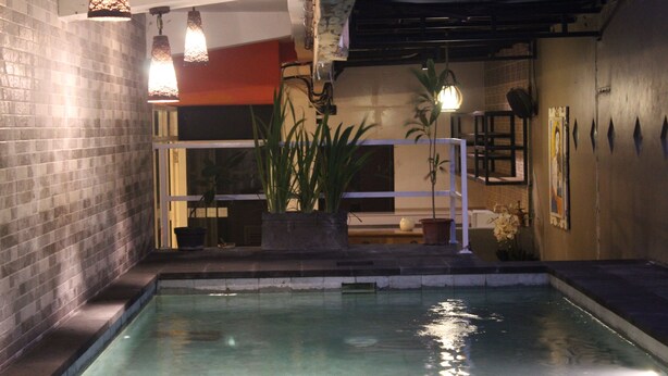 A swimming pool with a tiled border, a potted plant, and hanging pendant lights. - Mahatma Residence (Denpasar)