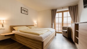 A hotel room with a wooden bed, a nightstand, a chair, and a wardrobe. - Appart Residence Kristall by Skinetworks (Saalbach-Hinterglemm)