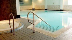 An indoor swimming pool with a clear water surface, a metal handrail, and tiled flooring.