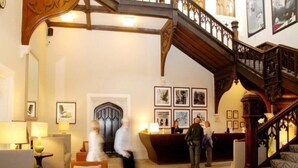 A lobby with a wooden staircase, a reception desk, and framed artwork on the walls.