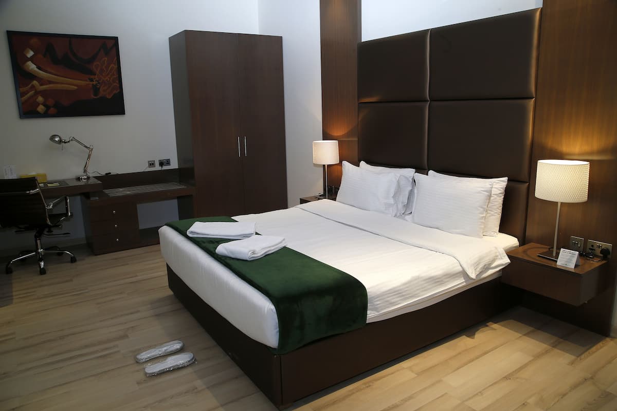 A neatly made bed with a green throw, a wooden desk with a chair, a large wardrobe, and two bedside lamps.