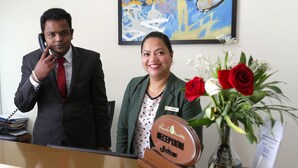 Un comptoir d’accueil avec une plaque nominative, un téléphone et un vase de fleurs.