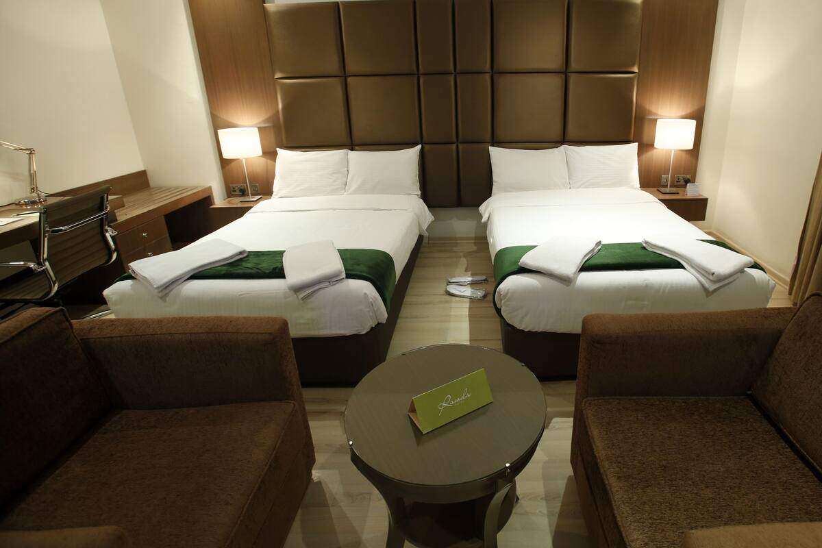 A hotel room with two beds, a small round table with a name card, and two armchairs.
