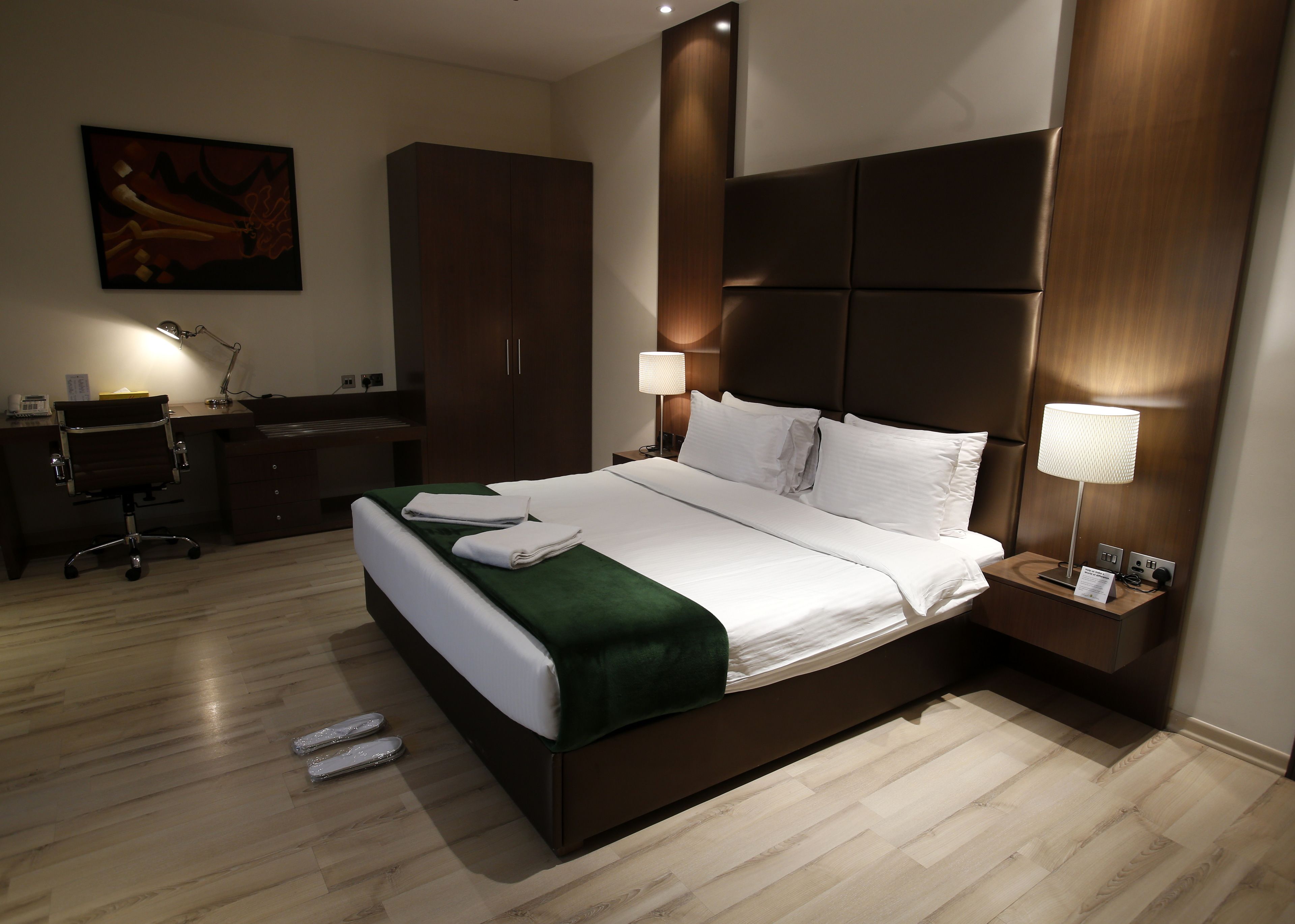 A hotel room with a large bed, a desk, a chair, and a wardrobe.