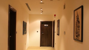 Un couloir d’hôtel avec un tapis à motifs, des portes en bois et des œuvres d’art encadrées accrochées aux murs.