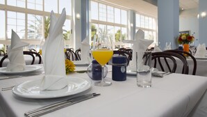A dining table set with white napkins, plates, cutlery, a glass of orange juice, and a candle.