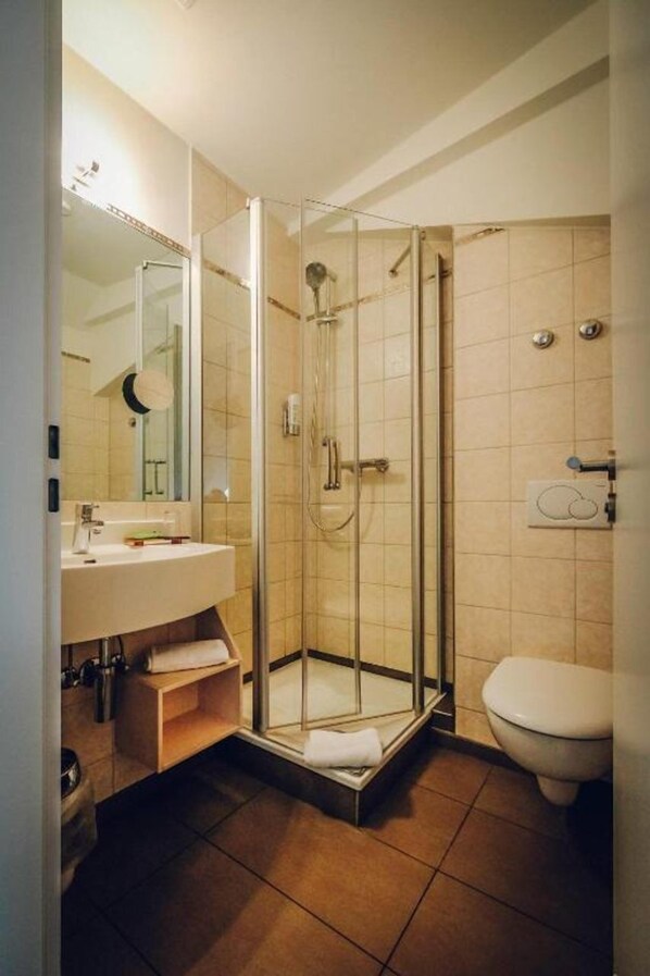 A modern bathroom with a glass-enclosed shower, a sink with a mirror, and a toilet. - Europa Bamberg (Bamberg)