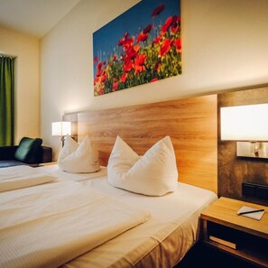 A hotel room with two beds, a painting of flowers, a green curtain, and a nightstand with a lamp. - Europa Bamberg (Bamberg)