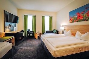 A hotel room with a bed, two chairs, a desk, a television, and a painting.