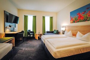 Una habitación de hotel con cama, dos sillas, un escritorio, televisor y un cuadro.
