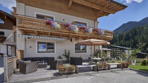 An outdoor patio with wicker furniture, a wooden pergola, and flower boxes. - Pension Gabi (Saalbach-Hinterglemm)