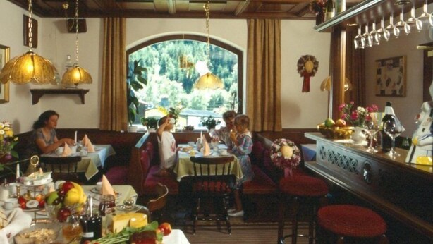 A dining area with a large window, multiple tables, and hanging lamps. - Pension Gabi (Saalbach-Hinterglemm)