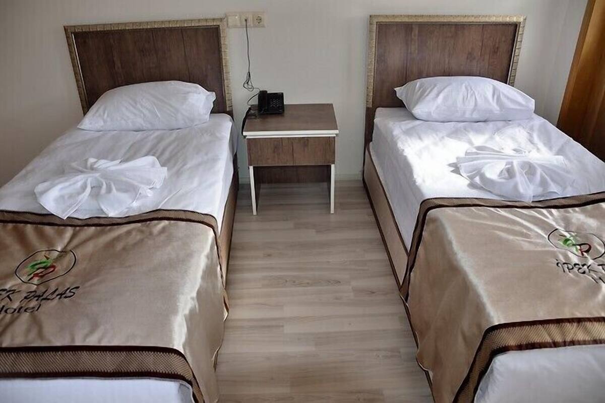 Ein Hotelzimmer mit zwei Einzelbetten, einem kleinen Nachttisch mit Telefon und Holzboden.