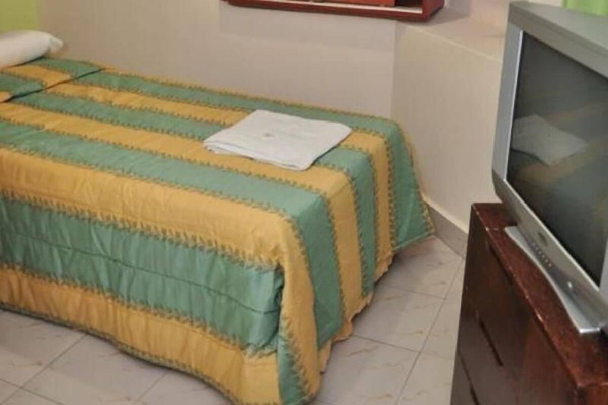 A bedroom with a bed covered in a striped blanket, a television on a wooden stand, and a white pillow on the bed.
