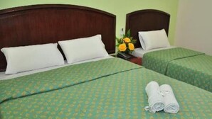 Ein Hotelzimmer mit zwei Einzelbetten, beide mit einem grün gemusterten Bettbezug und weißen Kissen. Dazwischen steht ein kleiner Tisch mit einer Vase voller gelber Blumen.