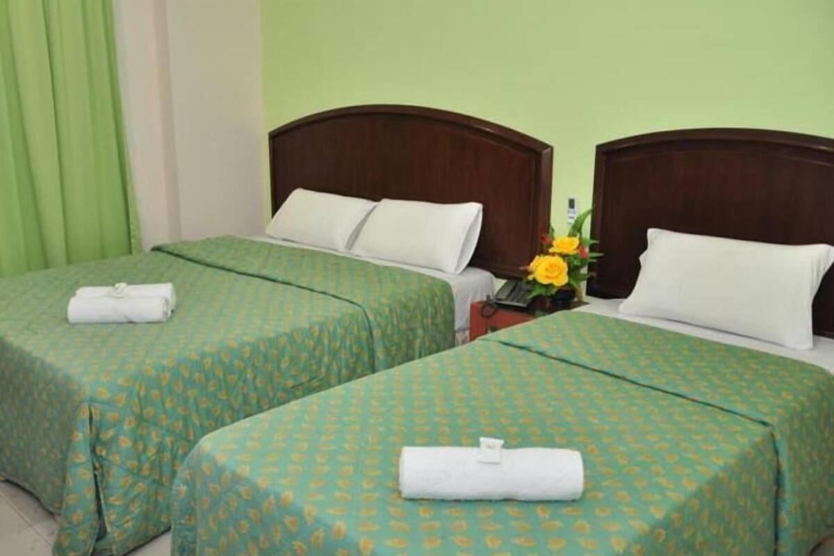 Two twin beds with green patterned bedspreads, white pillows, and rolled towels on each bed.