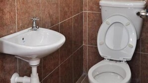 Ein Badezimmer mit weißem Waschbecken und WC, gefliesten Wänden und einem sichtbaren Rohr.
