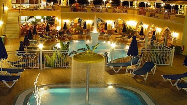 A pool area with lounge chairs and umbrellas, surrounded by a railing and a covered seating area with tables and chairs. - Hotel Pefkos Beach (Rhodes)