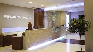 A reception desk with a wooden panel and a glass partition at the Pefkos Beach Hotel. - Hotel Pefkos Beach (Rhodes)