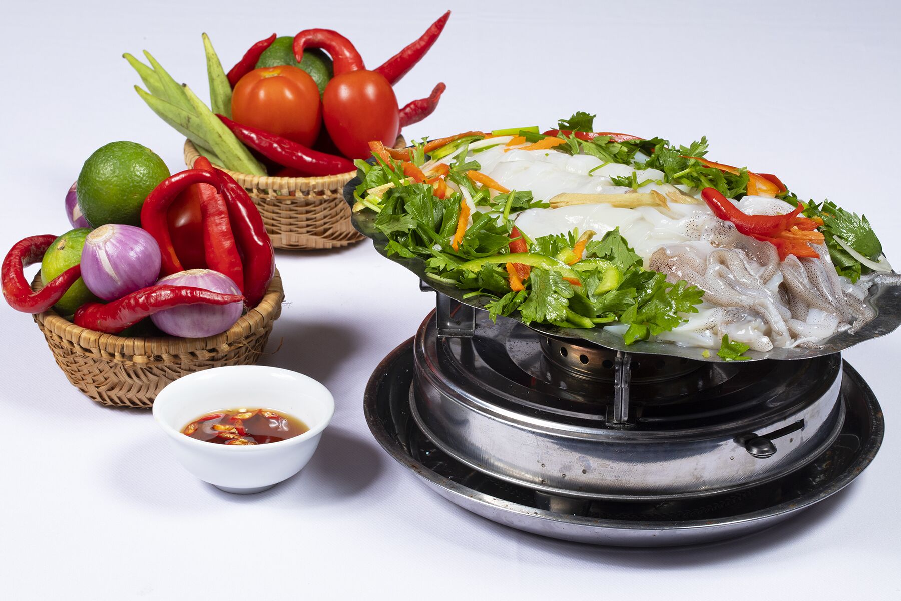 A bowl of noodle soup with vegetables and a small bowl of sauce.