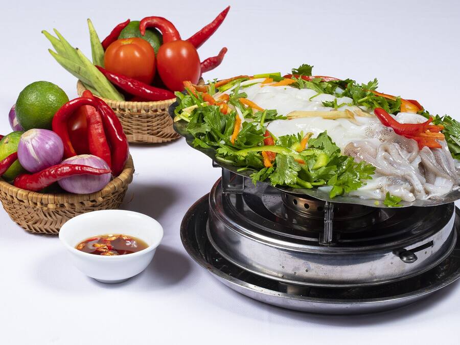 A bowl of noodle soup with vegetables and a small bowl of sauce.