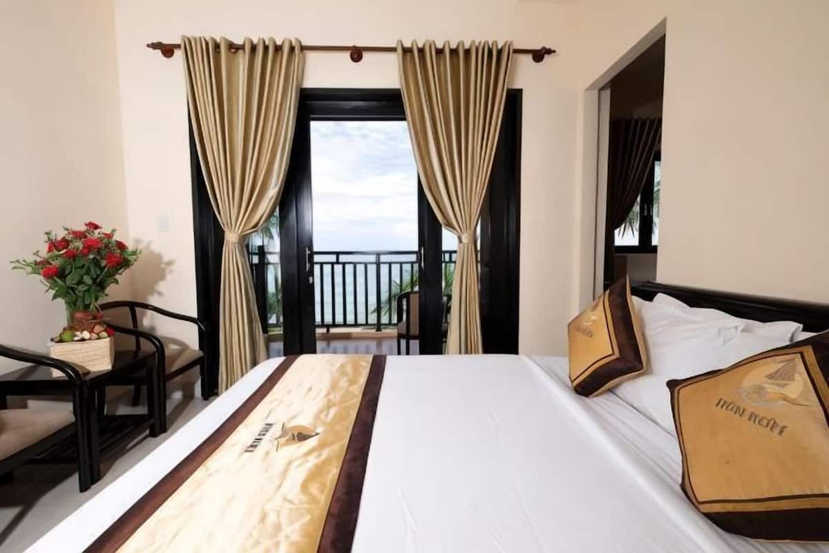Ein Hotelzimmer mit Bett, einem Sessel, einem kleinen Tisch mit Blumen und einem Balkon mit Vorhängen.