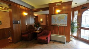 A lobby with a large world map, two red upholstered chairs, a potted plant, and a radiator.