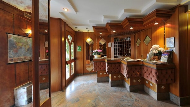 A hotel lobby with wooden paneling, a reception desk, and a large window. - Hotel Vela (Trento)