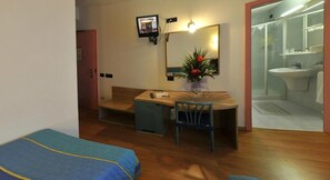 A small room with a wooden desk, a chair, a bed, a mirror, and a television.