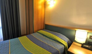 A hotel room with a bed, a nightstand, a lamp, and a curtain.